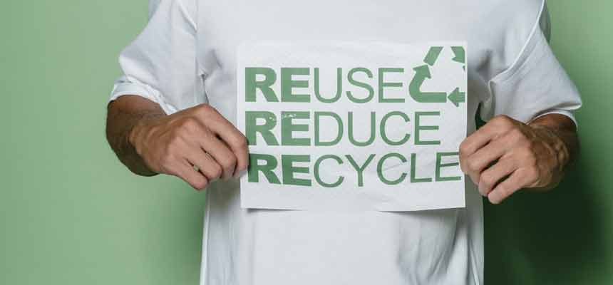 A person in a white t-shirt holding a sign saying "Reuse, Reduce, Recycle"