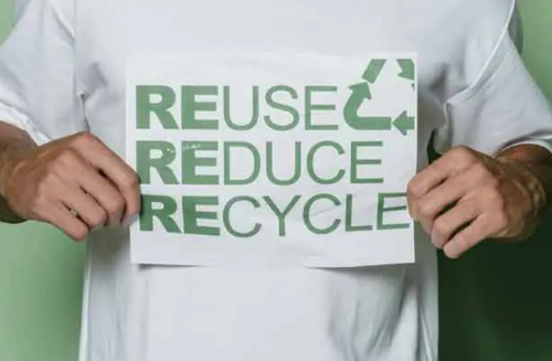 A person in a white t-shirt holding a sign saying "Reuse, Reduce, Recycle"