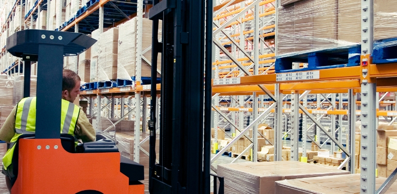 A worker using a forklift to move large heavy pallets