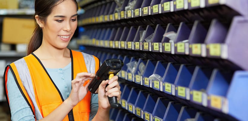 A person in a warehouse stood by a wall of picking bins