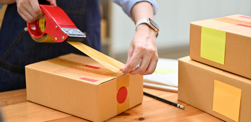 A person taping shut a cardboard postal box